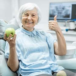 senior woman giving a thumbs up and holding an apple 