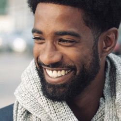 A young man wearing a scarf while outside and smiling after seeing his dentist in Louisville