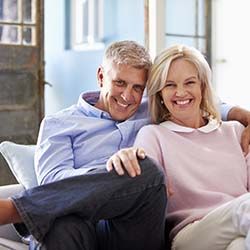 senior man and woman with dental implants in Louisville, KY sitting on their couch 