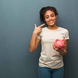 young woman holding a piggy bank and pointing to her smile 