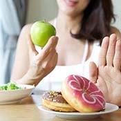 Woman holding apple and pushing plate of donuts away