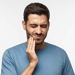 Man with a dental emergency in Louisville holding his cheek