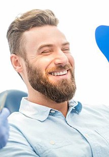 Male dental patient checking smile in handheld mirror