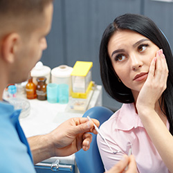 woman holding cheek looking at dentist
