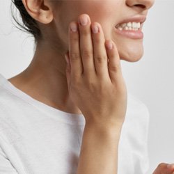 Woman in white shirt rubbing her jaw in pain