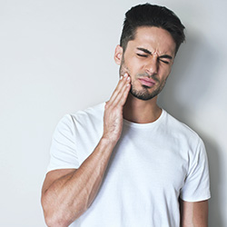man in white shirt holding cheek in pain