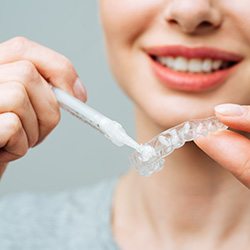 a woman putting whitening gel in a dental tray