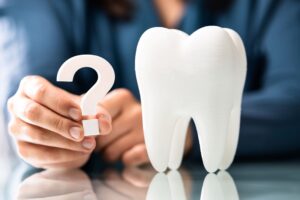 Someone holding a question mark next to a large model tooth