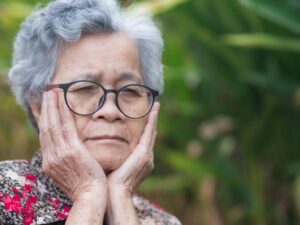 Older woman clasping her hands to her face in pain.